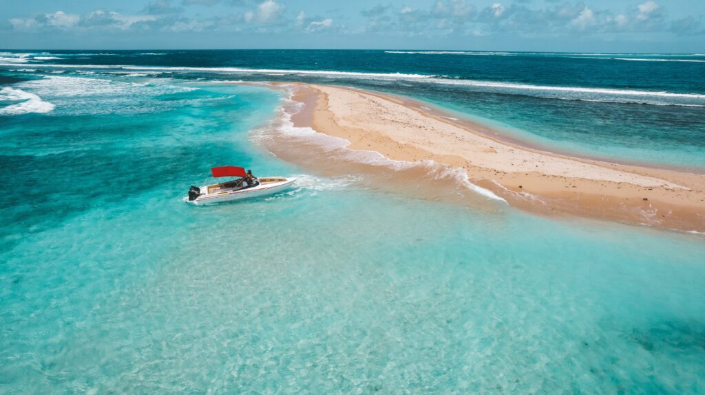 Widok na łódź płynącą w krystalicznie czystych wodach wokół Mauritiusa, z piaszczystą wyspą w tle.
